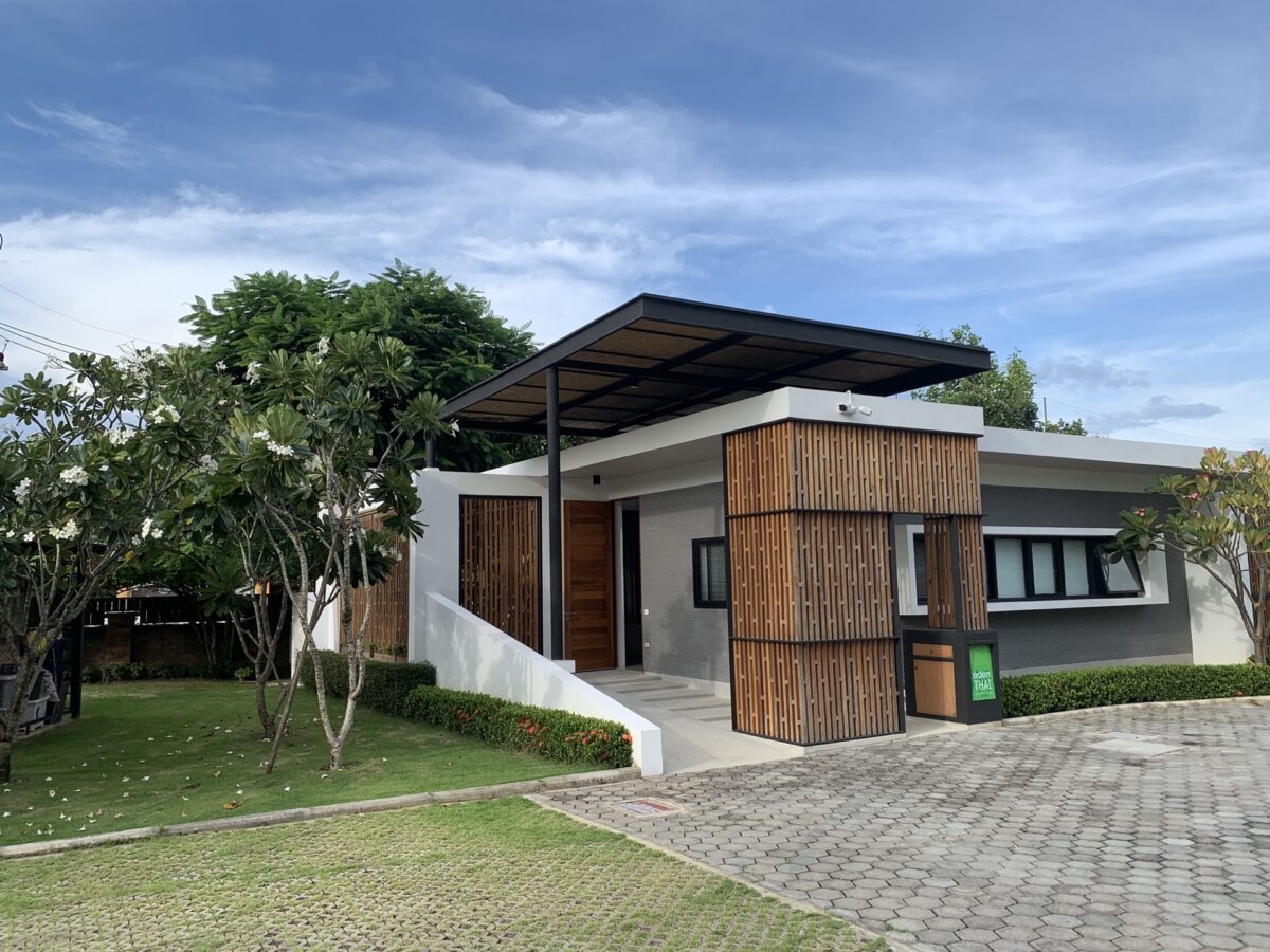 The 'Eden Thai' house, a recently built modern structure, boasts a wooden roof and a vibrant green lawn surrounding it.