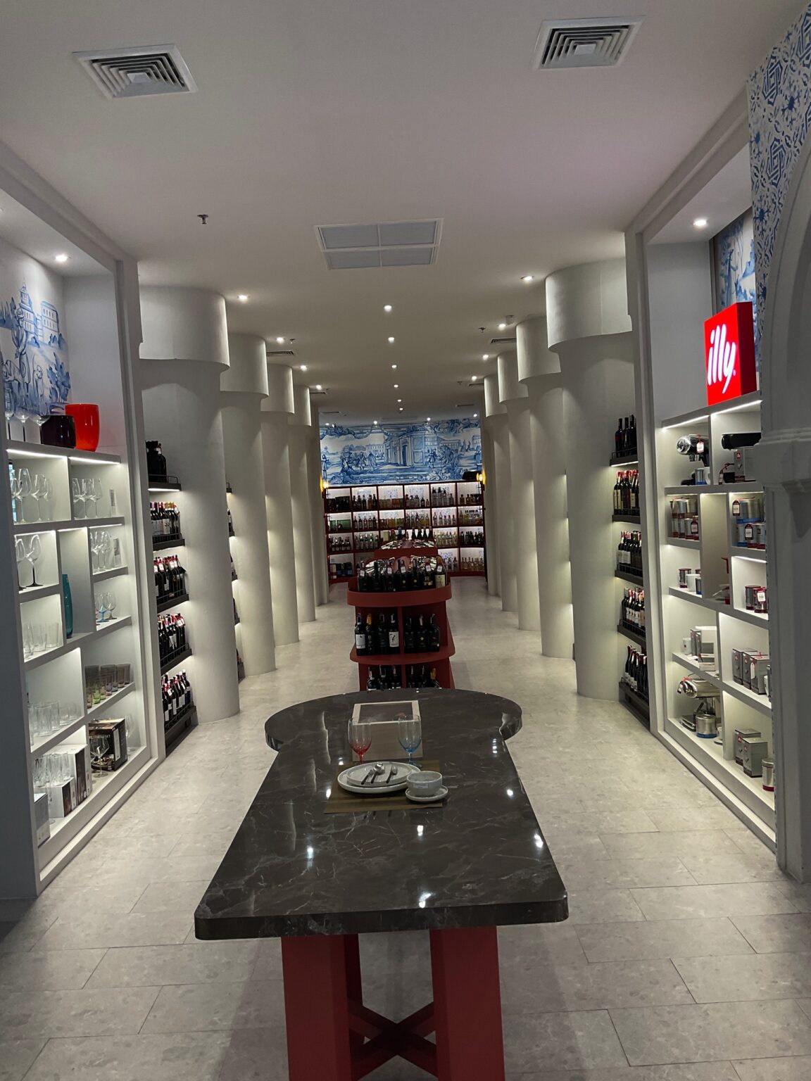 A renovated white 'illy' wine cellar featuring a long counter and shelves filled with various wine bottles.