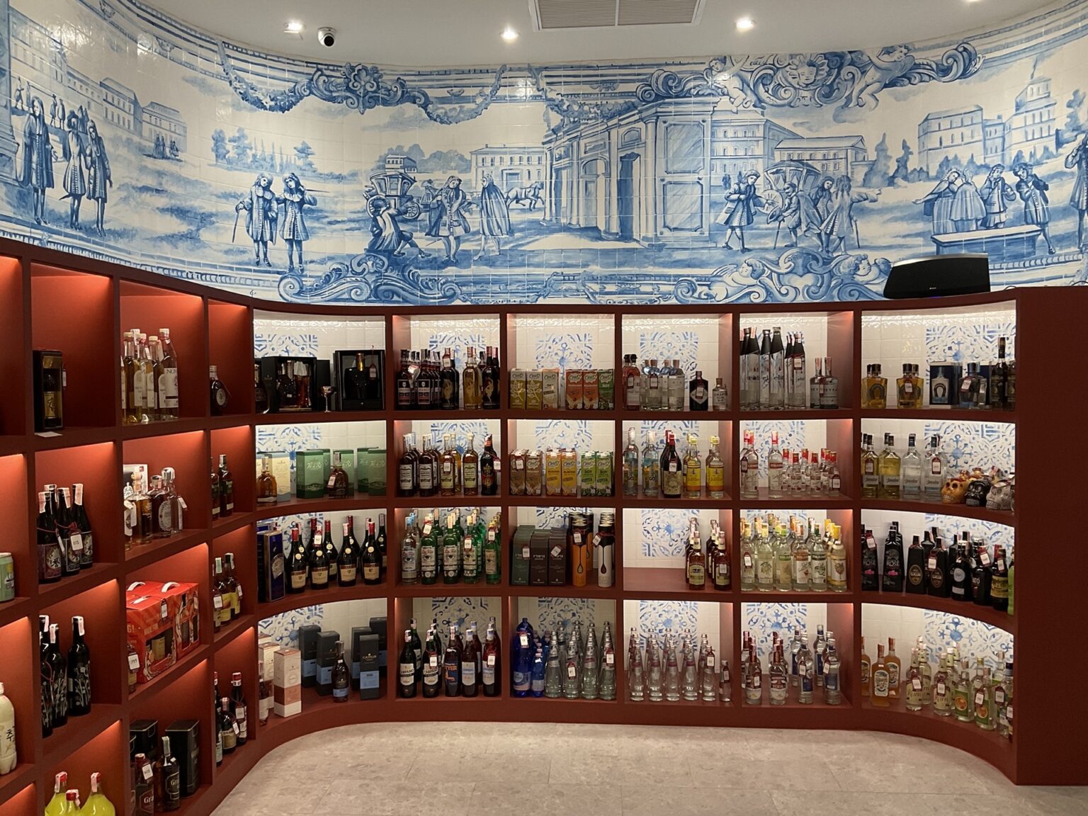 A renovated wine cellar featuring a wooden shelf displaying numerous bottles of alcohol beneath a beautifully painted fresco