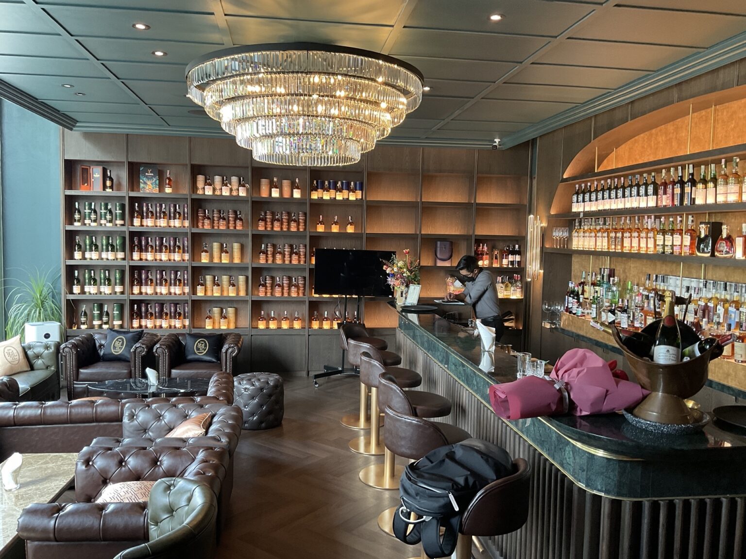 A stylish bar featuring leather couches and an elegant chandelier, showcasing the renovated Phill Collection bar and counter.