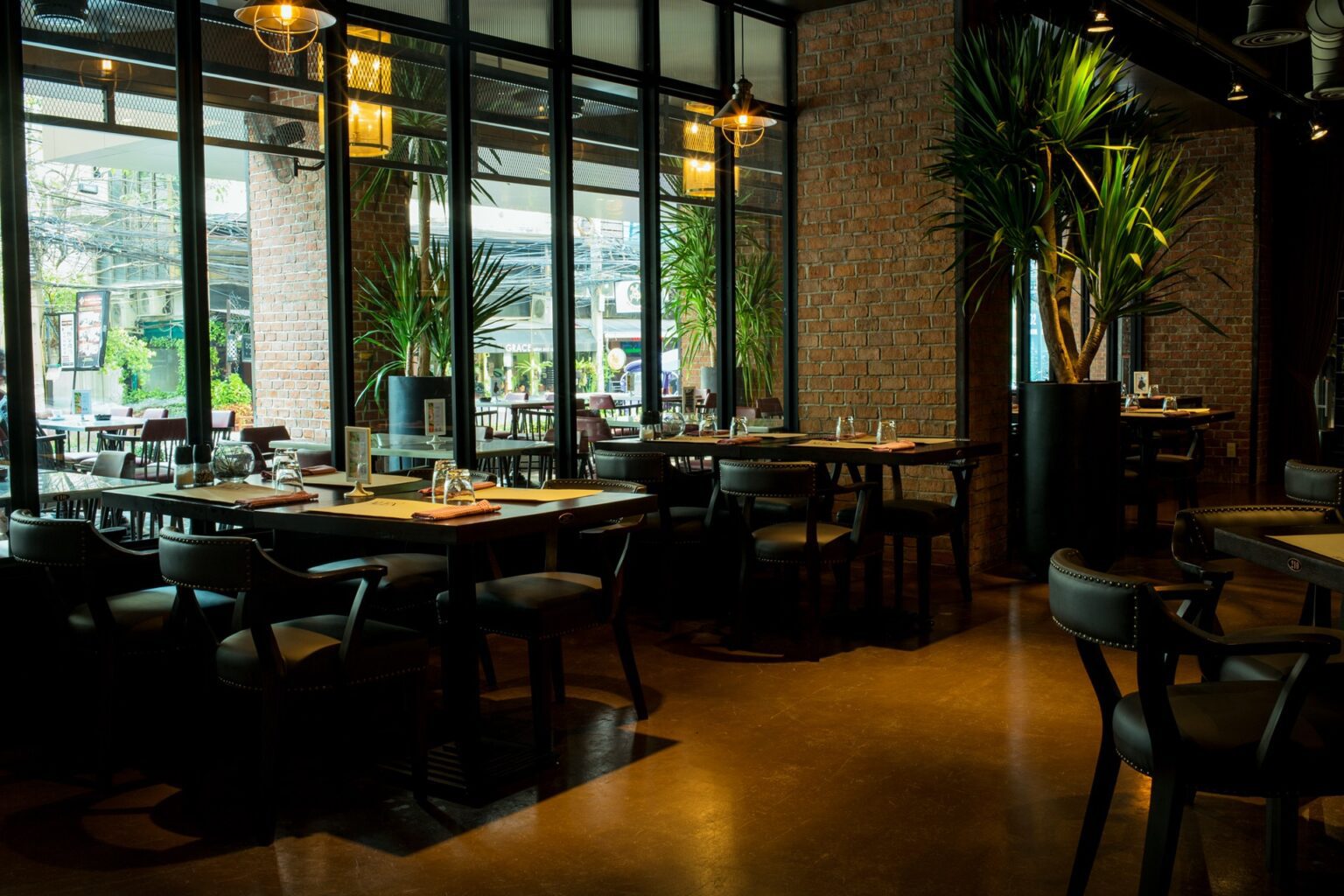 Interior of a renovated restaurant featuring wooden tables, numerous chairs, plants, and stylish black-framed windows.