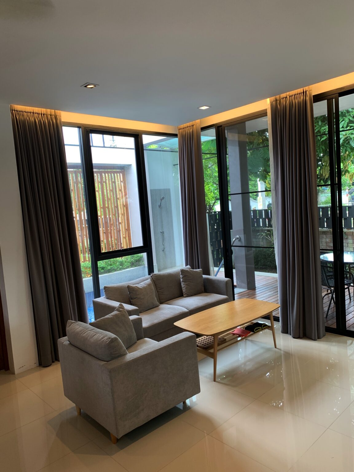 A bright living room in the 'Eden Thai' villa featuring a couch, coffee table, and sliding glass doors.