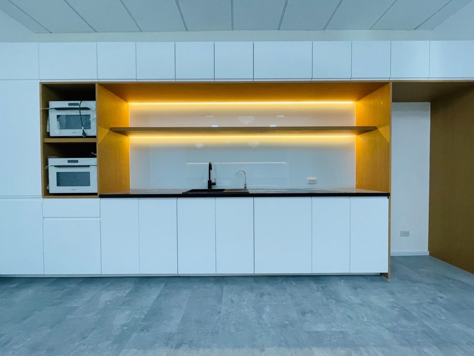 A bright kitchen with white cabinetry and soft yellow lighting, highlighting the renovated carpentry in the common area.