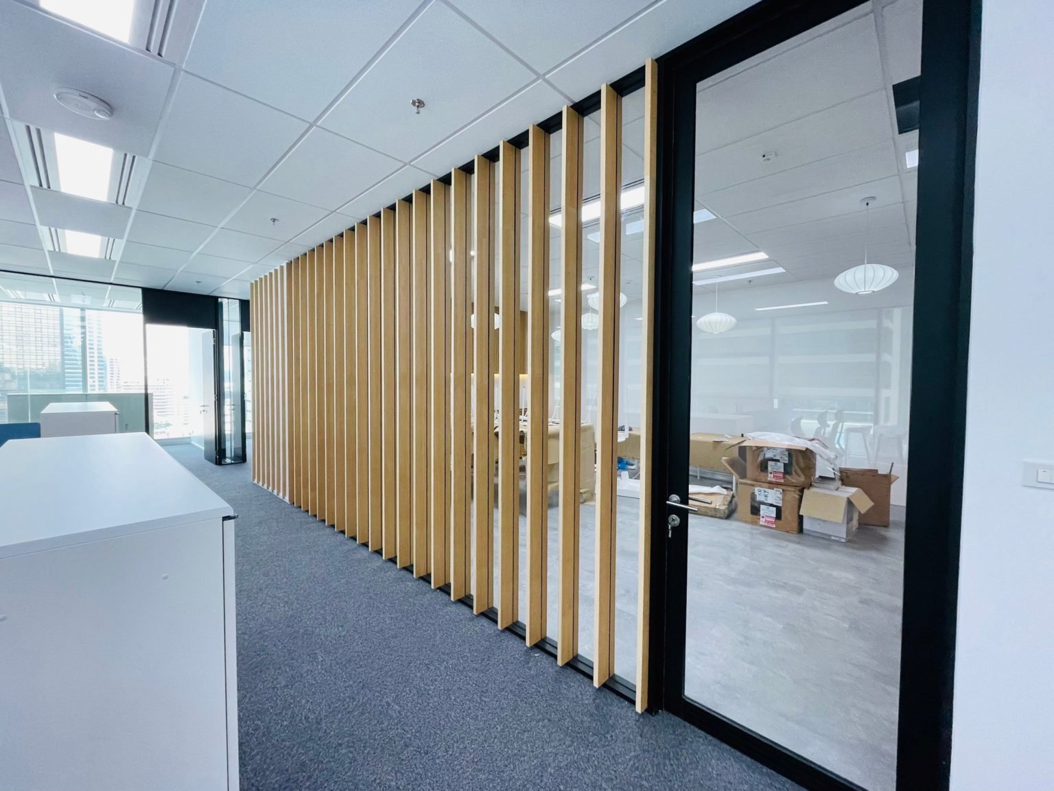 A contemporary office featuring wooden partitions and glass doors, showcasing an open space with renovated carpentry elements.