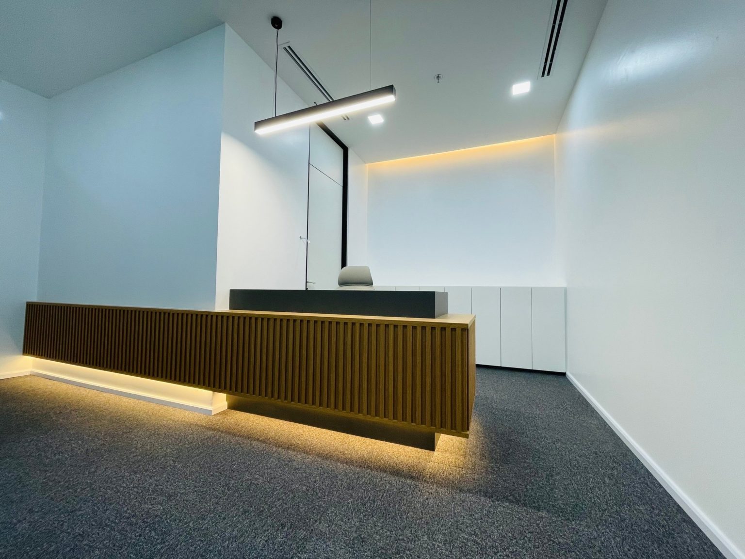 A modern office featuring a renovated reception desk with stylish lighting, showcasing contemporary carpentry design.