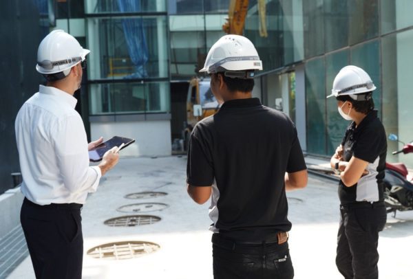 Our Project'Sabai locally experienced team, equipped with hard hats, stands on a renovation site in front of a large building, surrounded by construction tools.