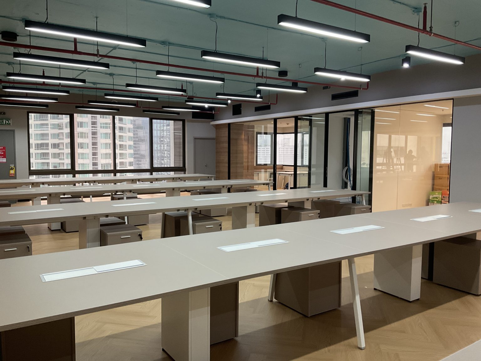 A freshly renovated office devoid of occupants, displaying contemporary desks and tables in a spacious layout.