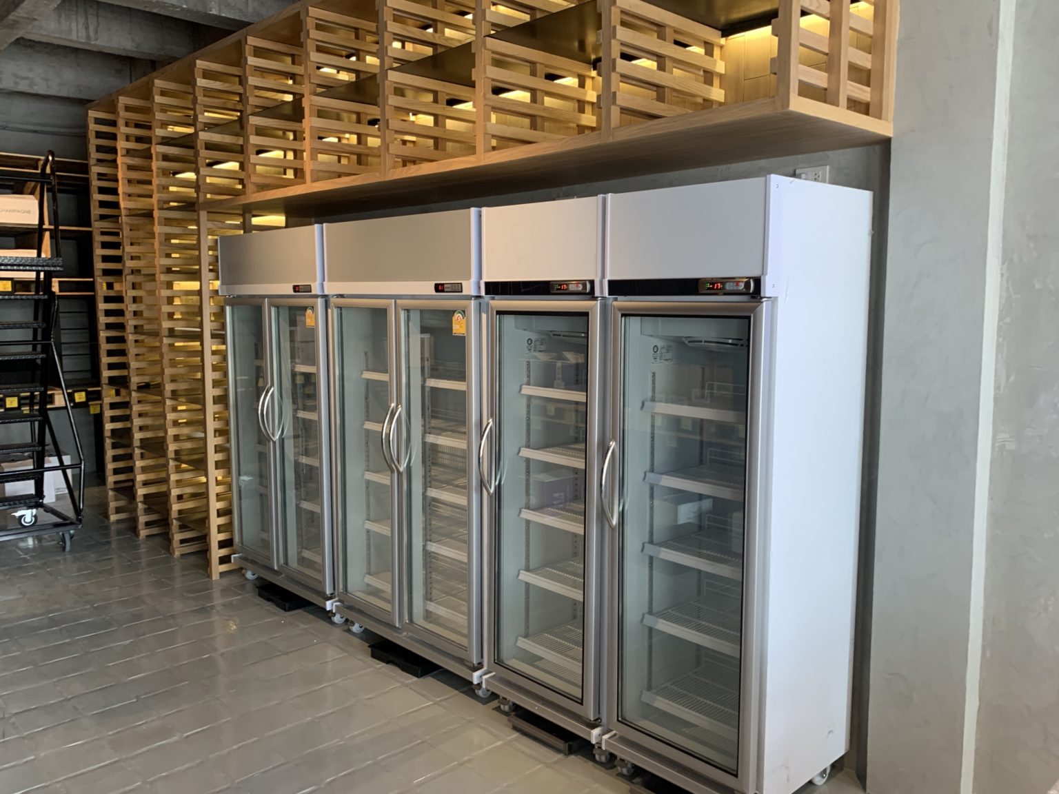 A modern refrigerator in a retail shop room featuring newly renovated wooden shelves for an organized display