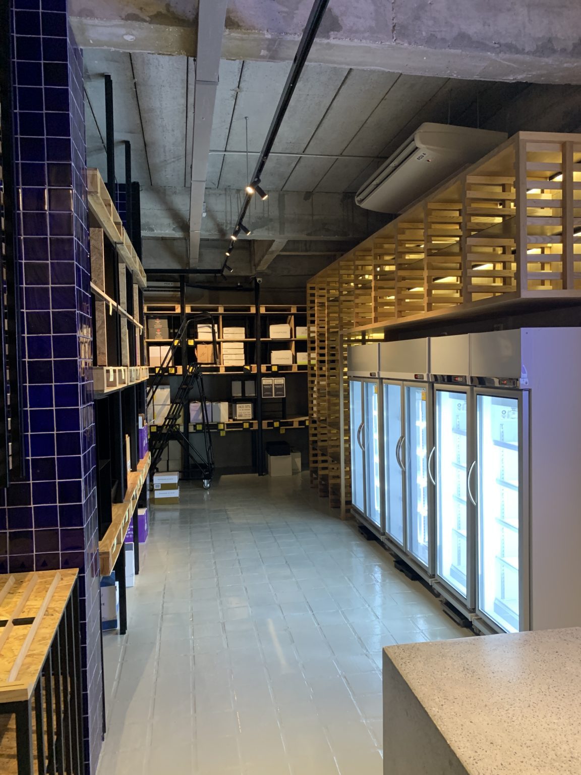 Interior view of a renovated retail shop featuring new fridges, wooden shelves and blue wall tiling.