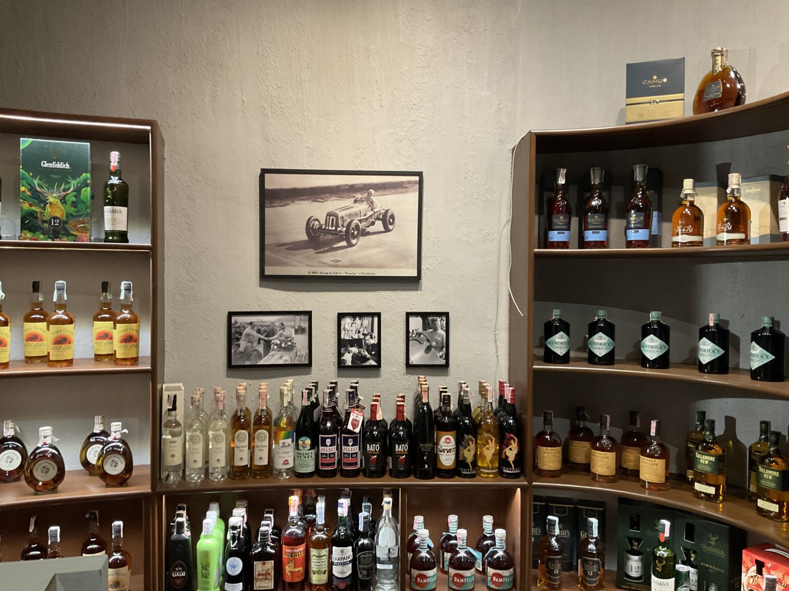 A renovated Italian wine showroom featuring an array of liquor bottles and decorative posters with cars on the wall.