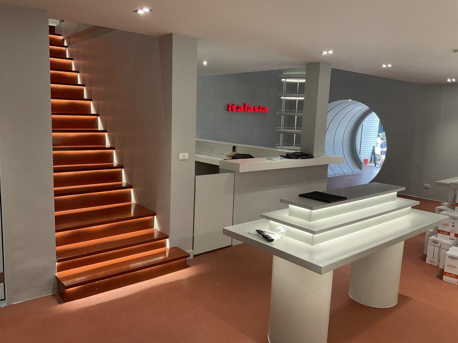 An elegant stairway in a renovated Italian wine showroom, highlighted by a prominent lighted sign above it.