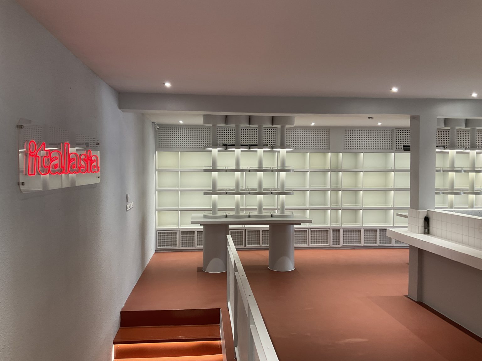 A renovated Italian wine showroom featuring a long hallway lined with shelves and a sign on the wall.