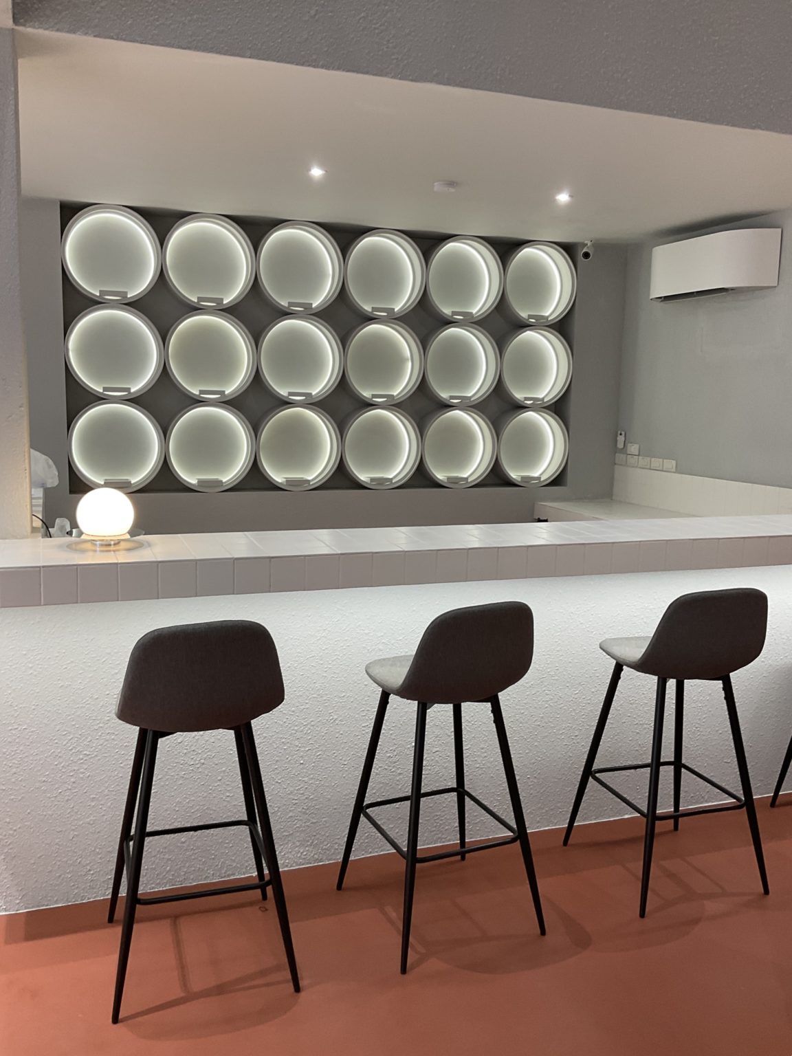 A renovated Italian wine showroom featuring a white counter and several chairs, creating an inviting bar atmosphere.