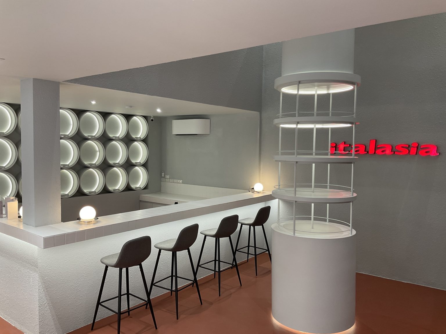 Interior of a renovated Italian wine showroom showcasing a white counter and a few chairs, perfect for wine tasting.