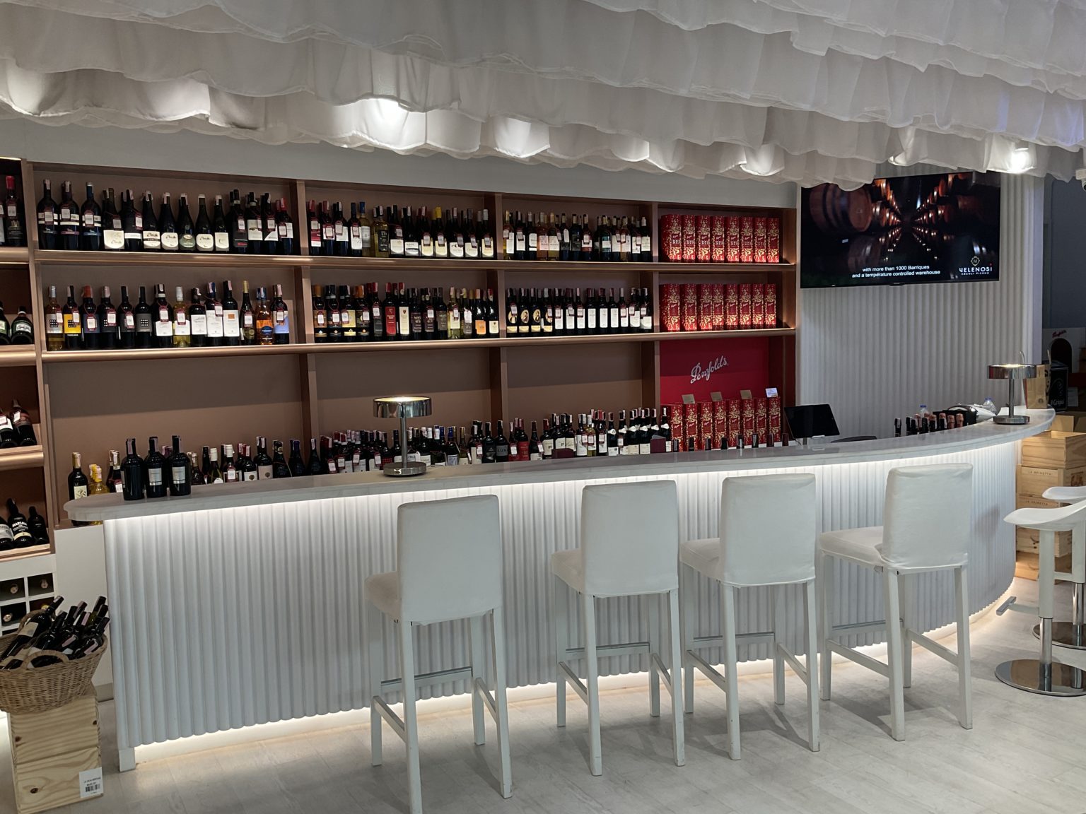 A stylish Italian wine showroom with white stools and shelves, elegantly displaying a diverse collection of wines.