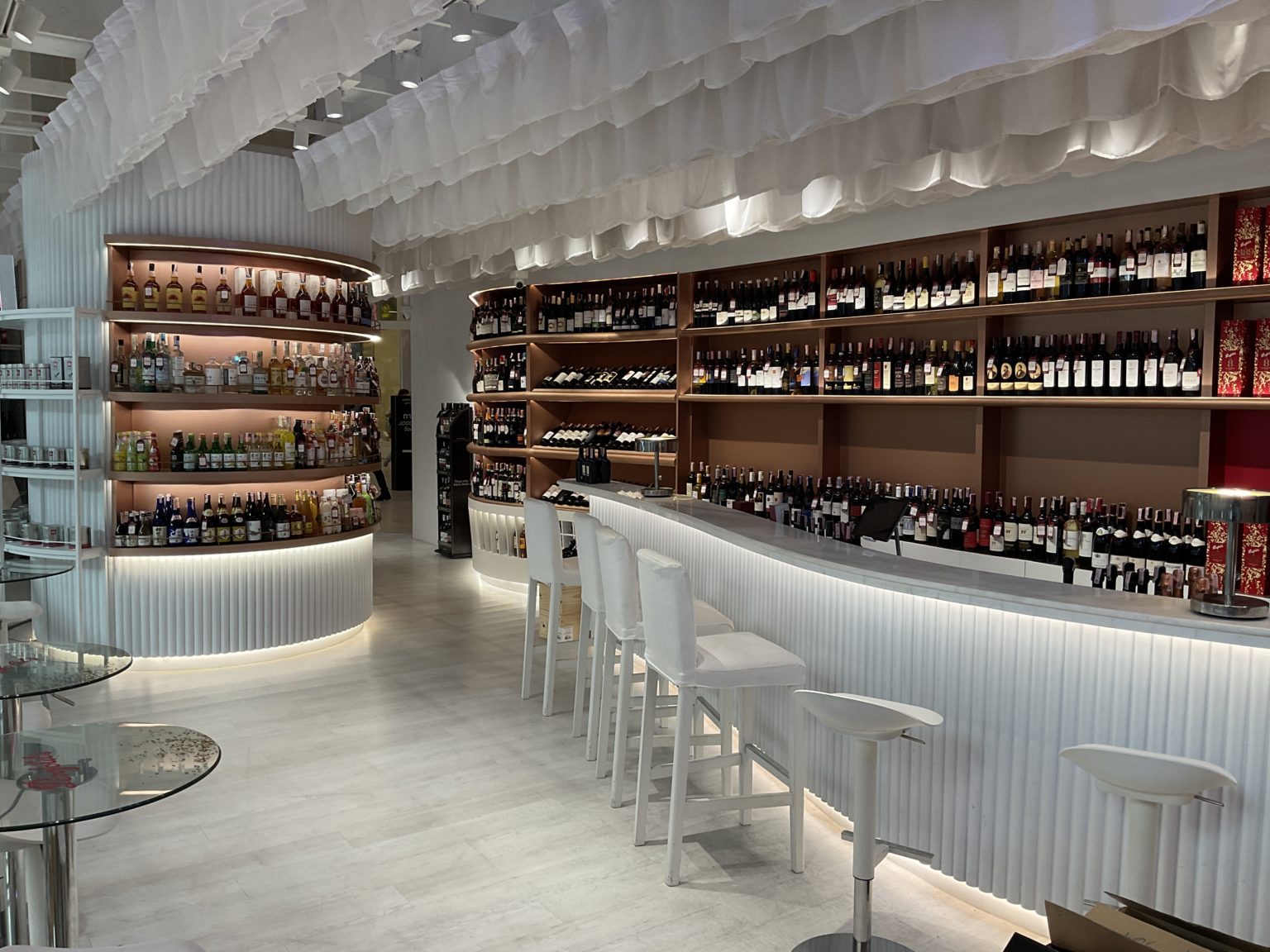 A renovated Italian wine showroom featuring white stools and elegant shelves filled with various wine bottles.